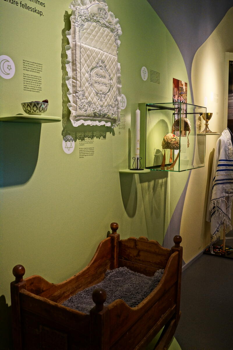 Bildet fra utstillinga Fra vogge til grav. På bildet ser du en vogge, en brit mala-pute, et dåpslys og dåpsluer.