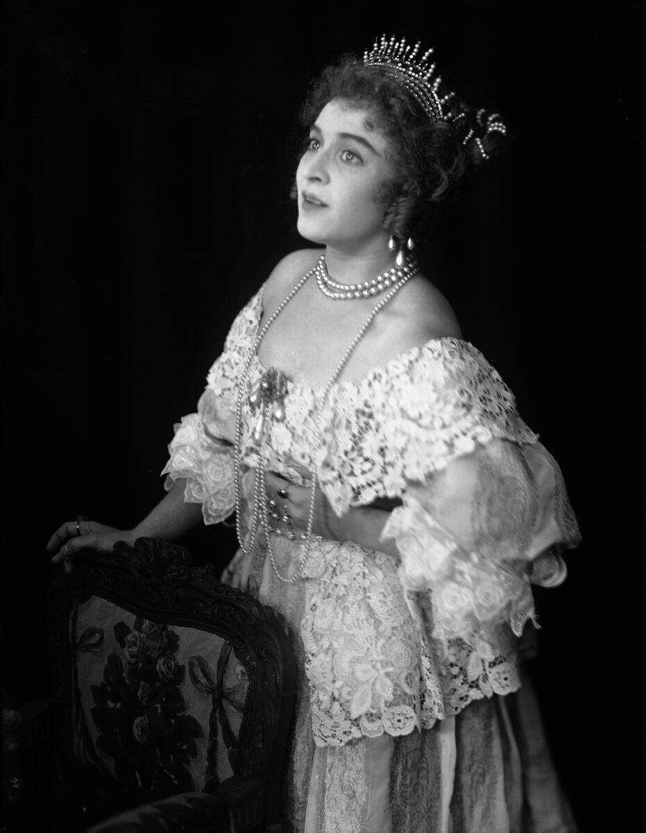 Portrett av skuespilleren og sceneinstruktøren Gerda Ring. Hun poserer i en ballkjole. med en tiara på hodet og med diverse perlesmykker.