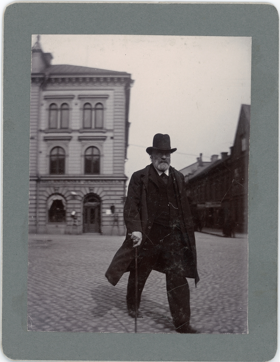 En man med hatt och käpp promenerar över Stora torget, Uppsala