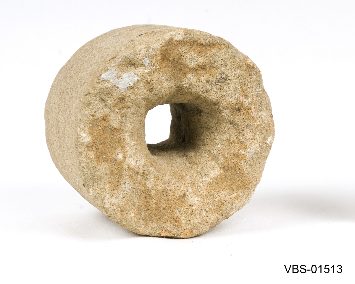 Sylinderformet slipestein. Den har et sentralt hull, med en firkantet seksjon, som gjennomborrer steinen fra side til side.