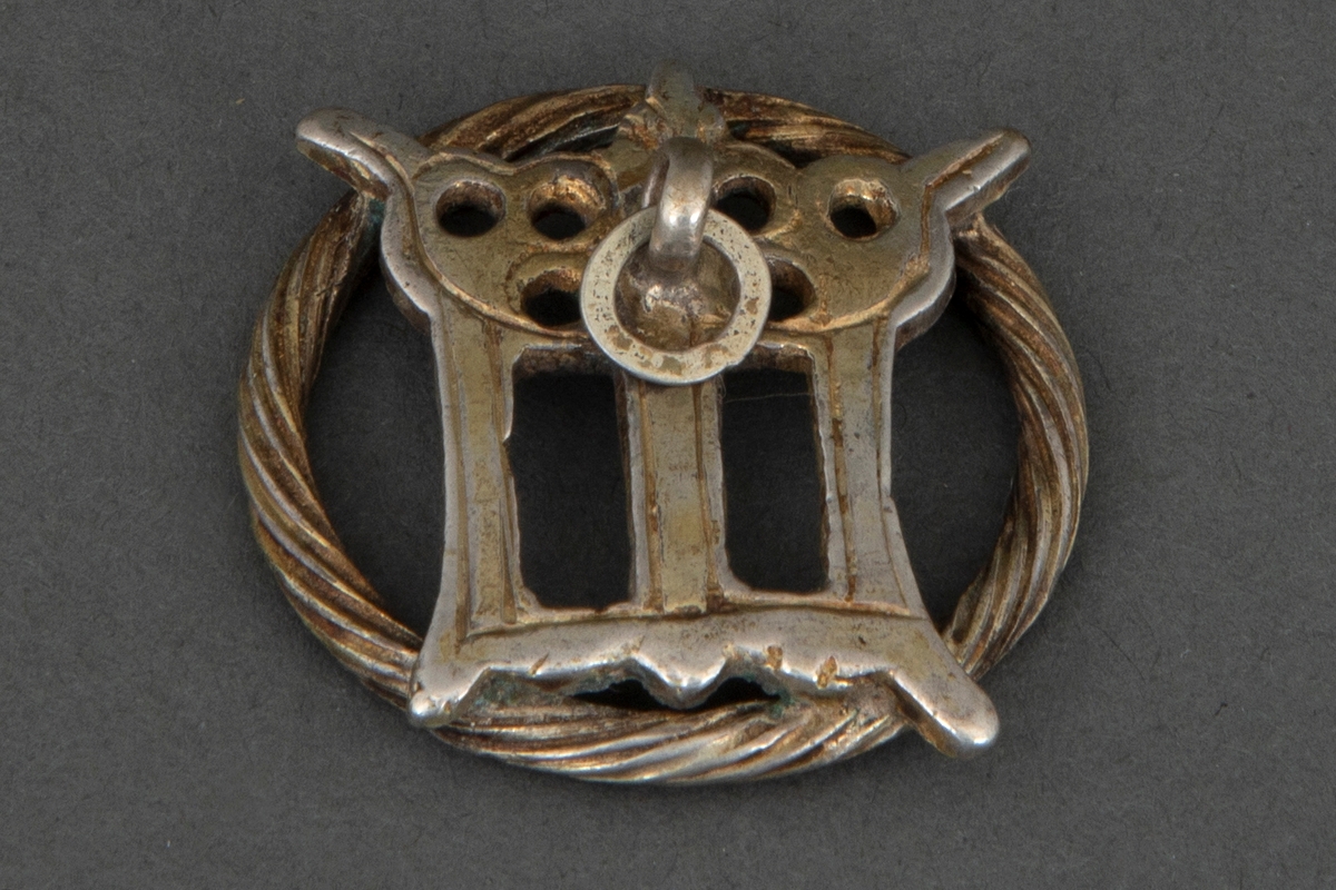Tre prydmaljer i forgylt sølv. Kraftig ring med påloddet gjennombrutt, og muligens, en sterkt stilisert utforming av kronet gotisk minuskel "m". Foran en bøyle med en nedhengende flat ring.