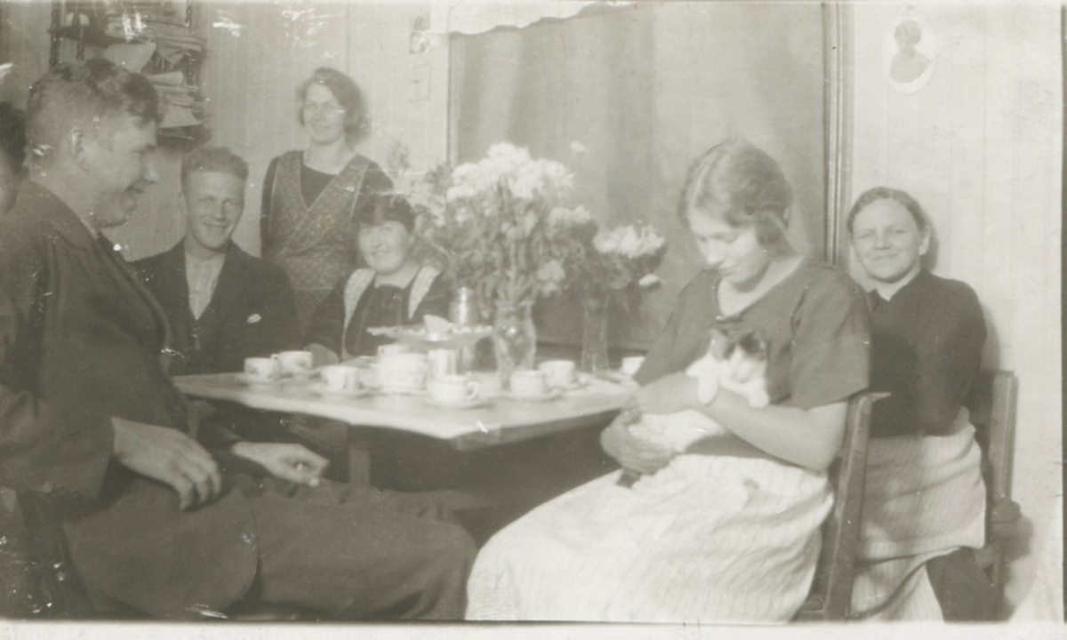 Sex personer sitter och fikar i "Nygård" Kållered Stom 1:3 på Gamla Riksvägen, okänt årtal. Från vänster: 1. Okänd man. 2. Okänd man. 3. Okänd kvinna (stående). 4. Elin Pettersson (1901 - 1988, gift Rothvall). 5. Okänd kvinna med katt. 6. Carolina Gustafsson (1873 - 1949).