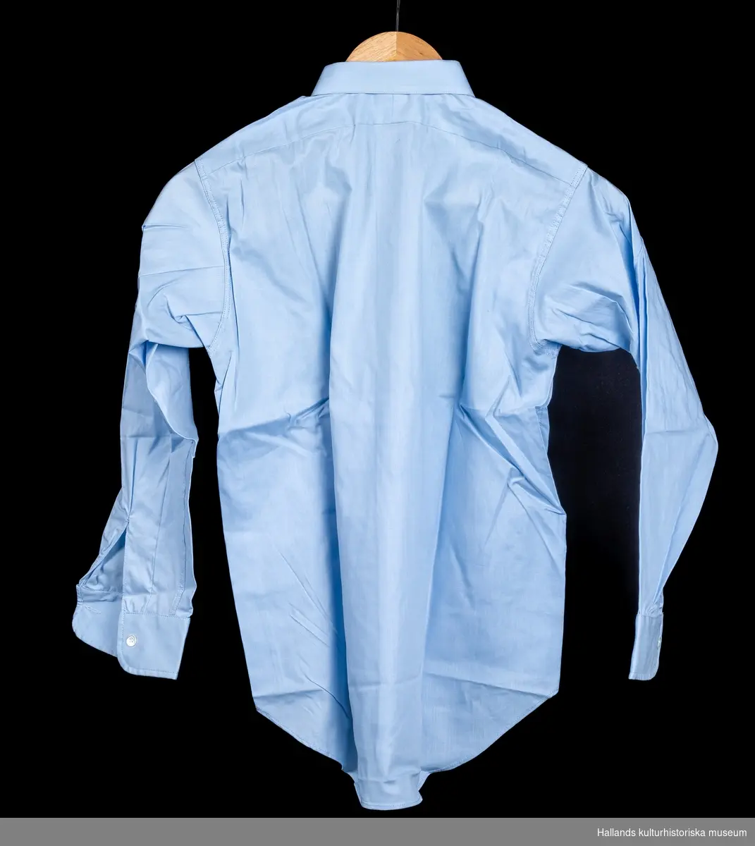 Skjorta avsedd för pojke. a) Ljusblå bomull. Rak modell med knäppning fram. Märkt: "Prins Bore storlek 31. Kokas ej, stärkes eller strykes fuktig". b) Beige bomull. Rak modell med knäppning fram. Märkt: "Prins Bore storlek 31, kokas ej, stärkes eller strykes fuktig". c) Stödkartong av papp, överkroppsformad. Boreskjortan med bättre passform.d) Stödkartong av papp, rektangulär form med upphöjt stöd för kragen. e) Skjortkartong med lock, rektangulär form. Märkt: "Aktiebolaget Melka skjortor". a) Längd 66 cm. Bredd 38 cm. b) Längd 66 cm. Bredd 38cm. c) Längd 29,5 cm. Bredd 21 cm.d) Längd 29,5 cm. Bredd 20,7 cm.e) Längd 34 cm. Bredd 22,5 cm.