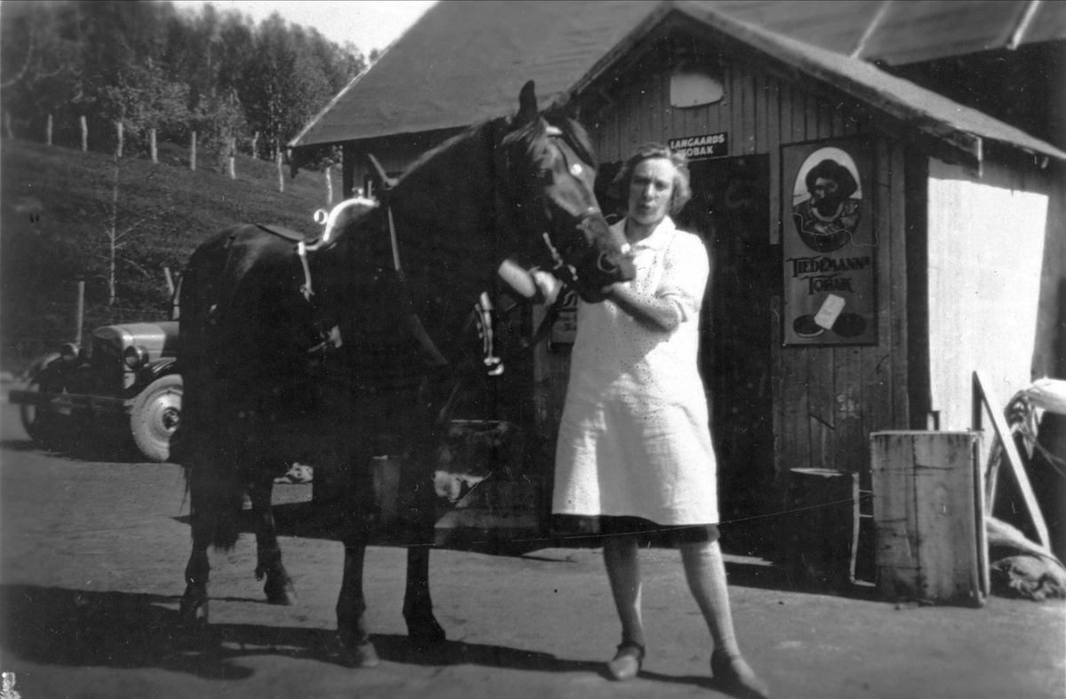 Kvinne og en hest, fotografert utenfor en butikk.