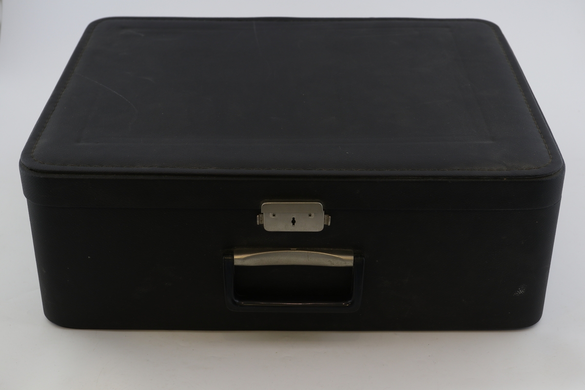 Kremhvit skrivemaskin med svart koffert. Ark i skrivemaskinen med programopplysninger for radio.