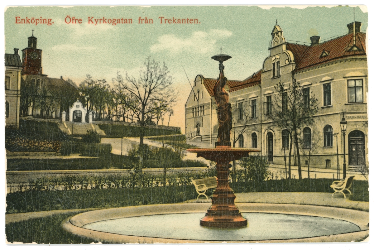 Vykort med motiv av övre Kyrkogatan och Kyrkbacken, Enköping. Fontänen i bild står i parken Trekanten och skulpturen i fontänen kallas Johanna.