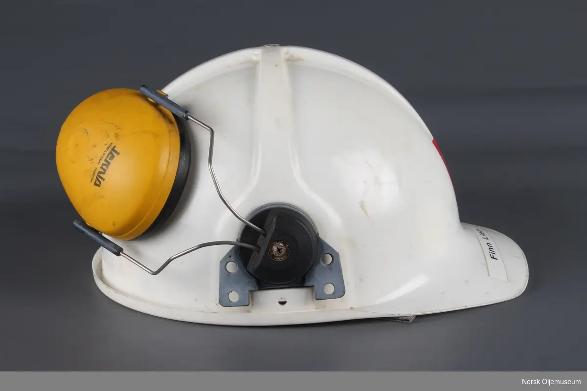 Hvit vernehjelm med hørselsvern. Hjelmen har Oljedirektoratet sin logo og navn til den som har brukt hjelmen plassert foran.