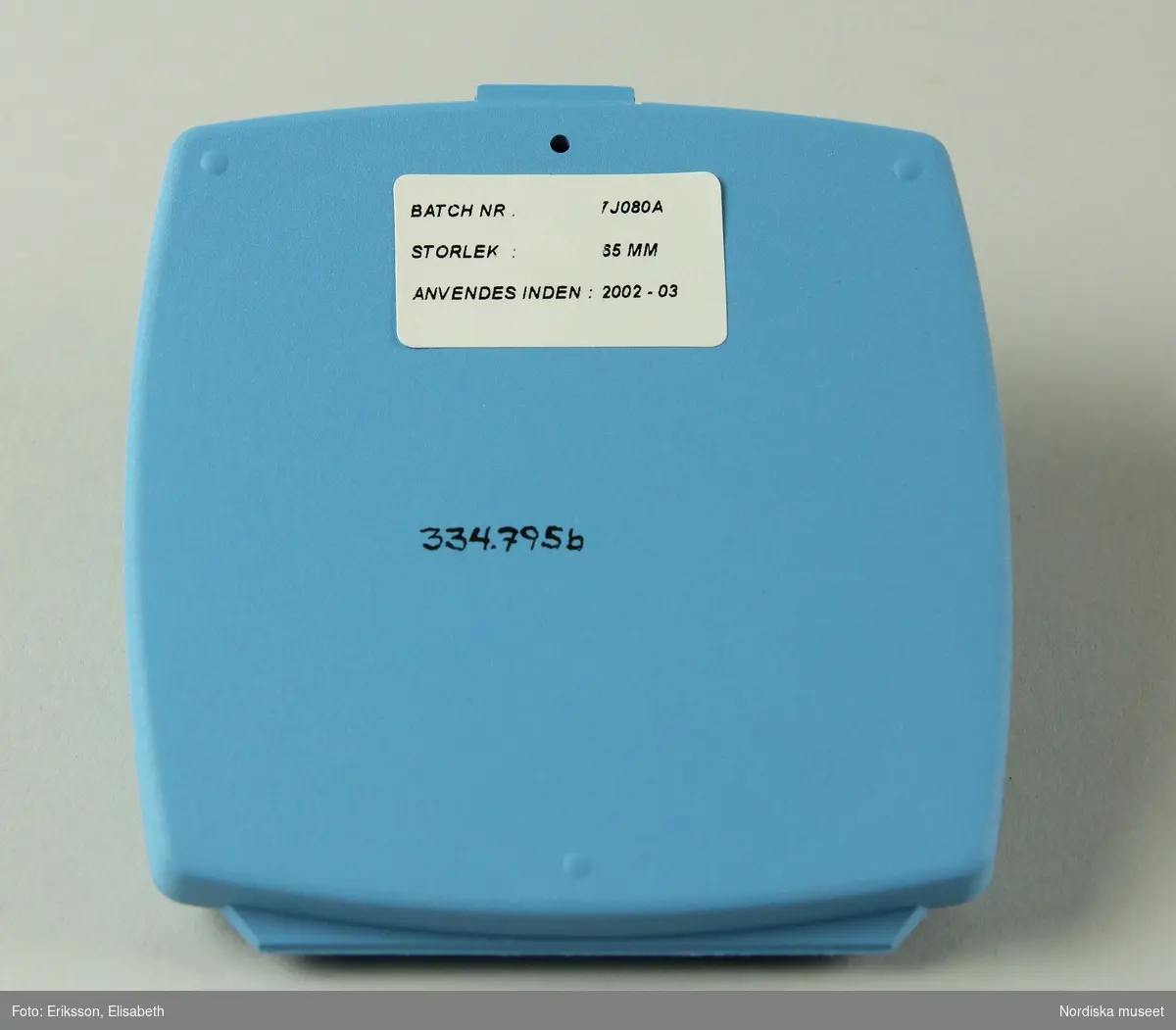 a) Pessarkopp i gulvitt gummi med b) förvarsingsask för pessar i blå plast, c) blå förpackning i kartong samt d) bruksanvisning.