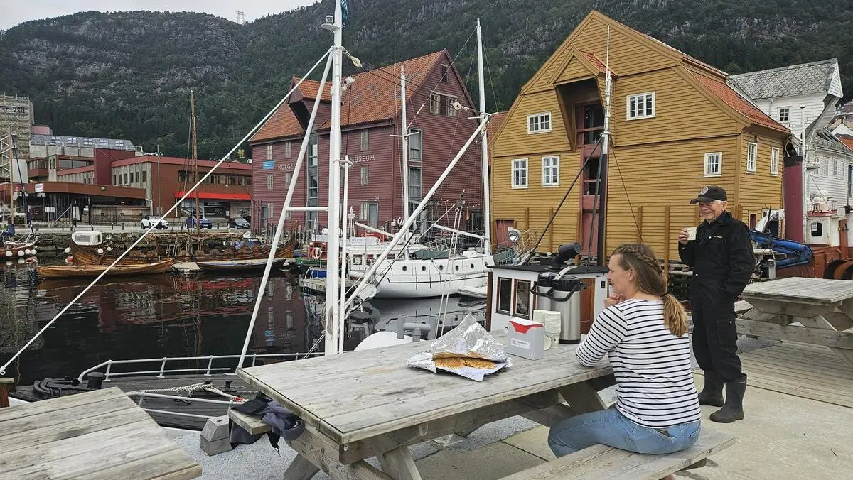 Bilder viser havnen, og en person som sitter med kaffekoppen og ser utover den, mens en annen står med sin kaffekopp