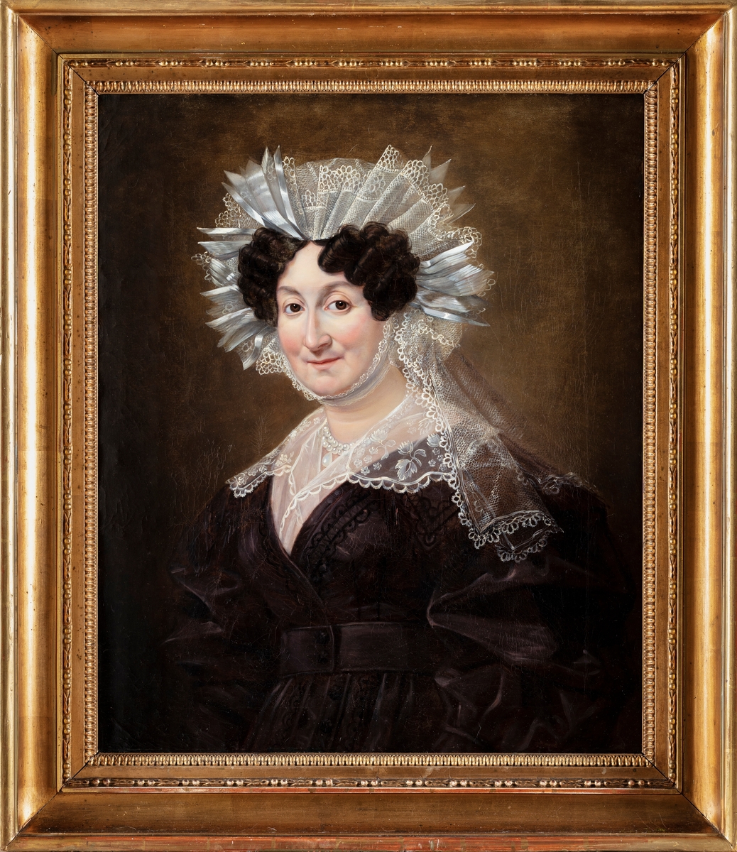 Porträtt av kvinna i svart klänning, vita spetsar runt huvudet och axlarna.