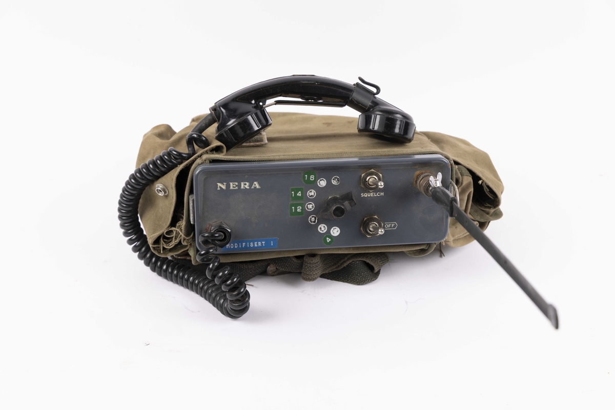 VHF-radio i tøyveske. Bærbar radiosender/mottaker i metall med antenne og telefonrør. Oppbevares i grønn tekstilveske med skulderreim.