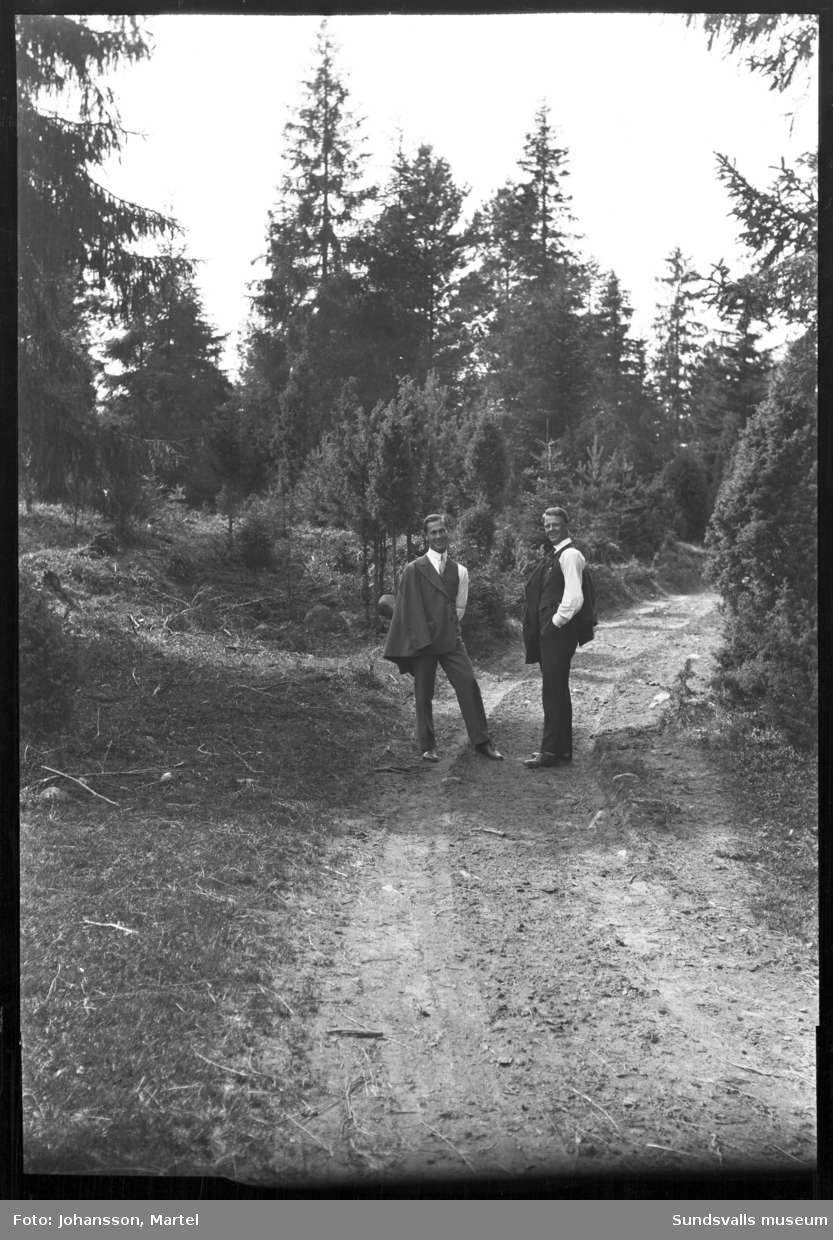 Två glada kostymklädda män på en skogsväg.