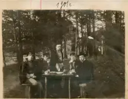 Fem menn fotografert under et måltid i skogen. De spiser og 