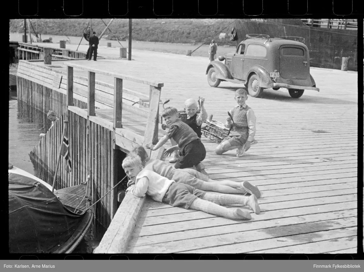Barn fisker på kai i Kirkenes. En av guttene holder en line ned til havet og viser fram en fisk

I bakgrunnen kan man se en bil med skiltnummer Y-3616, Chevrolet 1936 varebil (sedan delivery på originalspråket)

Foto antagelig tatt på slutten av 1940-tallet, tidlig 1950-tallet