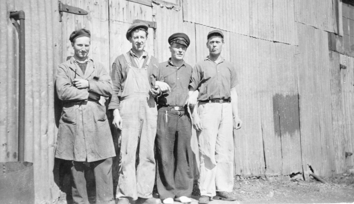 Gruppebilde : Fire menn oppstillt ved fyrhusveggen på Hestnes Hvalstasjon, Hitra.