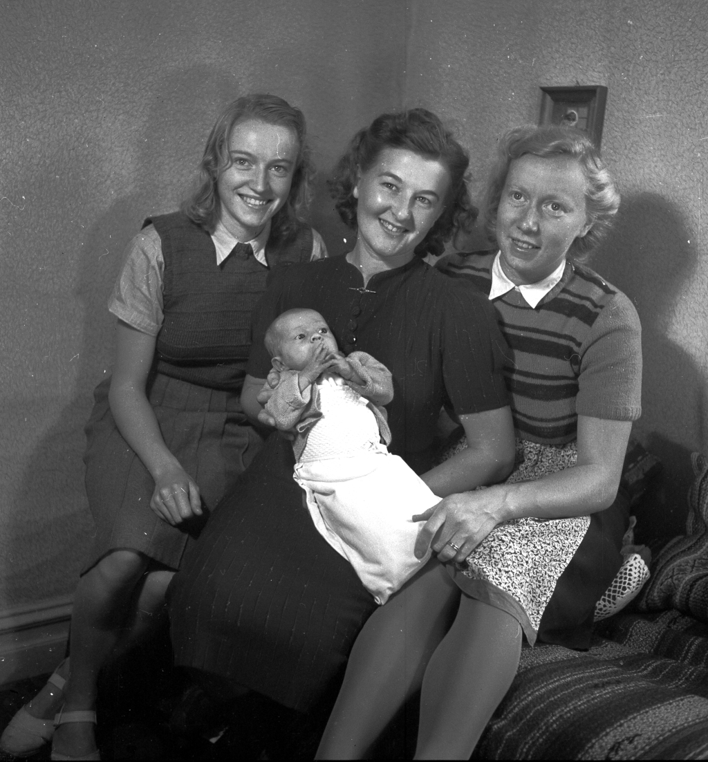 Tre kvinnor med en baby sittandes i en soffa.