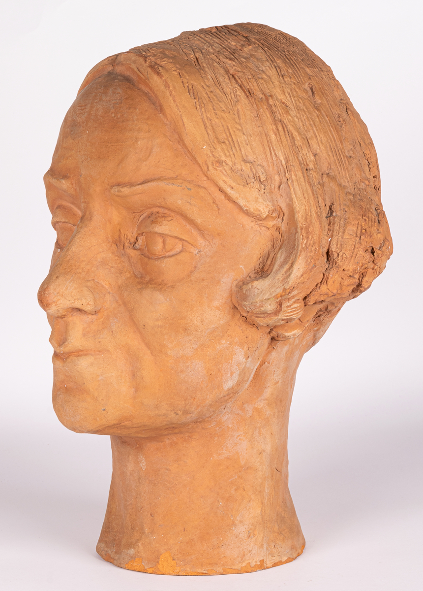 Porträttbyst i bränd lera av skulptör och keramiker Maggie Wibom, 1937. Bysten är med mycket stor sannolikhet ett självporträtt av konstnären, då den har flera karakteristika med Maggie Wibom, som frisyr, ögonbryn, ögon och näsa. Maggie Wibom har även i unga år, under tiden vid Tekniska skolan, utfört självporträtt i lera, vilket finns dolumenterat på foton.
