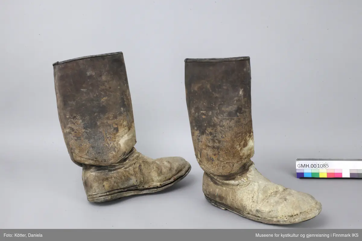 Ett par brune lærstøvler med høye skaft, som helt tydelig ble brukt til arbeid. Sålene er festet med spikre. Støvlene er i herrestørrelse og forurenset med mørtel og papir. 