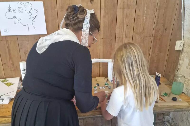 En dame kledd som Jensine Werenskiold hjelper en jente under en tegneskole.
