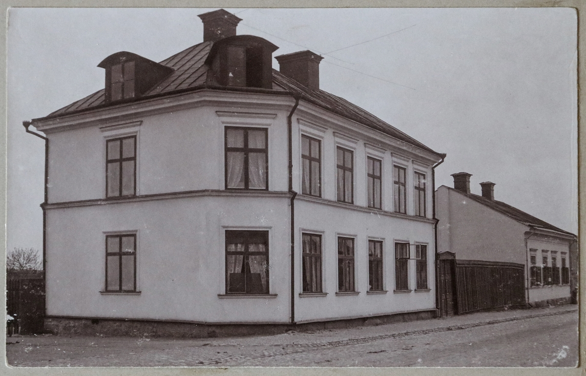 Motiv av byggnaderna på Eriksgatan 39 och 41, Enköping. Foto taget från Ågatan. Huset närmast kallades i modern tid för "blå huset" och drabbades av en hård brand 1992.

Vykortet tillhör vykortsalbum nr. EM06774:c. Denna sida i albumet har lossnat och ligger löst i pärmen.