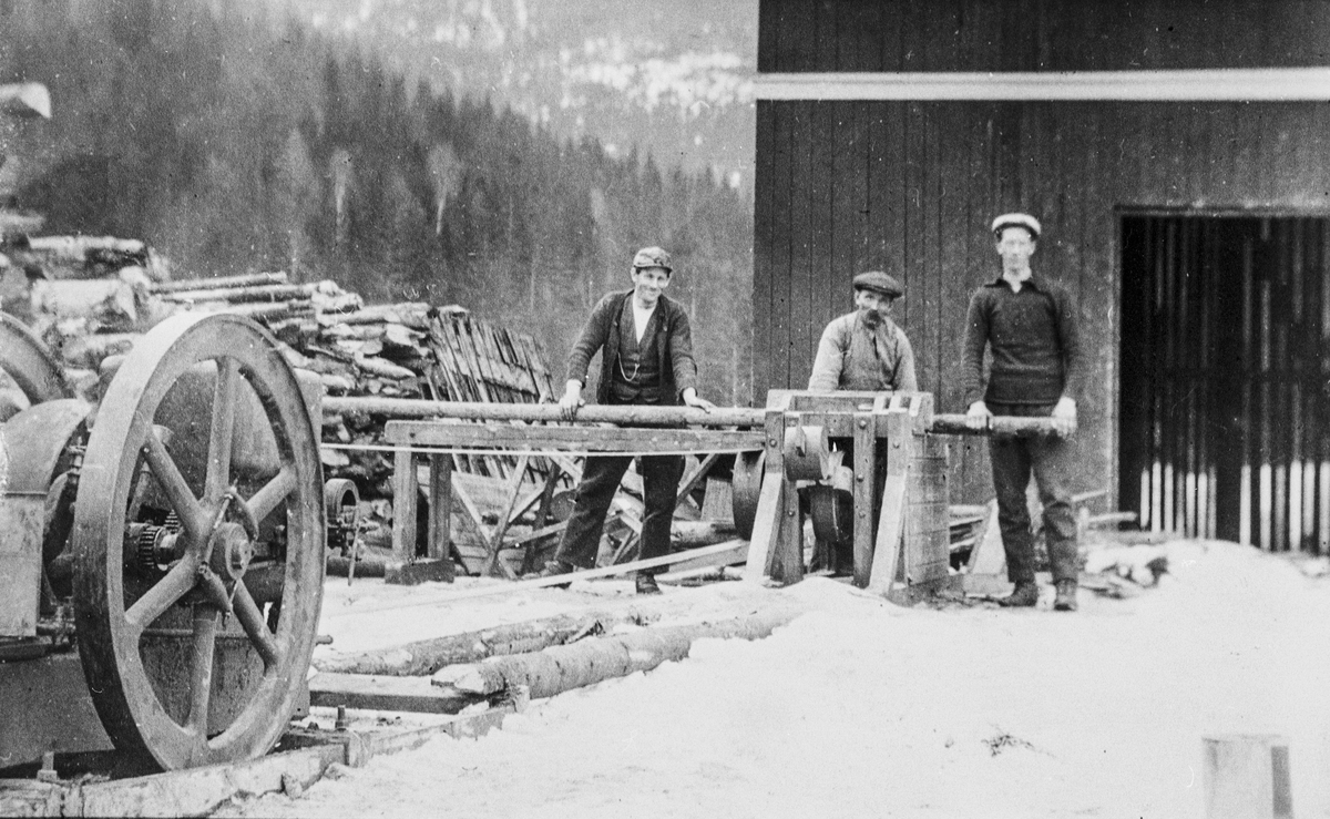 Vedkapping hos Kristoffer Kopseng med Lauson bensinmotor, på Søre Kopseng ca. 1915. Bildet viser Kristen og Engebret Kopseng, og den som kapper er antagelig Elling Enderud.