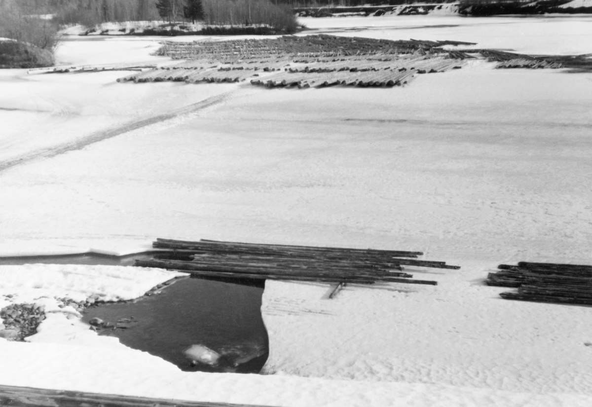 Tømmertillegging på elveisen under Indsetfossen i Glomma, i Strandygda i Elverum kommune i Hedmark. Fotografiet skal være tatt vinteren 1938. Det viser hvordan et tømmerparti var lagt i såkalte flakvelter på den snødekte isflata. Flakveltene besto av ett lag tømmerstokker som lå parallelt, men vinkelrett på to underlagsstokker. Underlagsstokkene skulle forebygge at tømmeret frøs ned i is og ble altfor fuktmettete etter eventuelle perioder med overvann. Fordelen ved denne tilleggingsmåten var at tømmeret ble veldig lett tilgjengelig for måling og merking. Her var det lett å se og kvalitetsvurdere hver enkelt stokk, med påfølgende «klaving» (diametermåling) og påslåing av kjøpermerker. Stokkene i flakveltene skulle ligge med de lengdemålene skogsarbeiderne hadde hogd på med romertall under apteringa oppovervendt, for å lette målernes arbeid. For å være noenlunde sikker på at tømmeret ikke ble altfor nedsnødd og nediset skulle det helst ikke legges tømmer i flakvelter for tidlig på vinteren. Denne tilleggingsmåten var arealkrevende, men det var jo ikke noe problem på ei bred elv som Glomma.