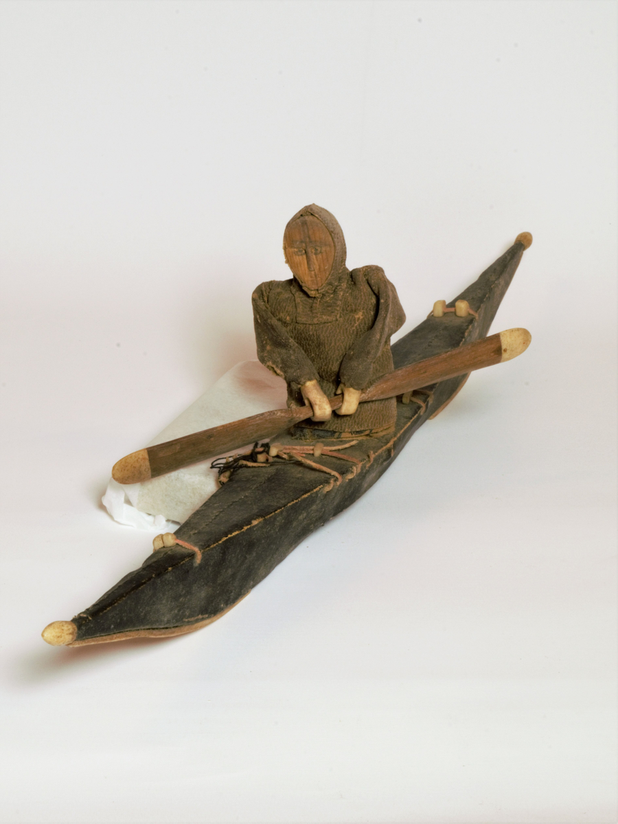 Sjømannsouvenir. Modell av kajakk med eskimo som padler. Kjøpt på Grønland av sjømann tilhørende Gabrielsens Rederi, Farsund
