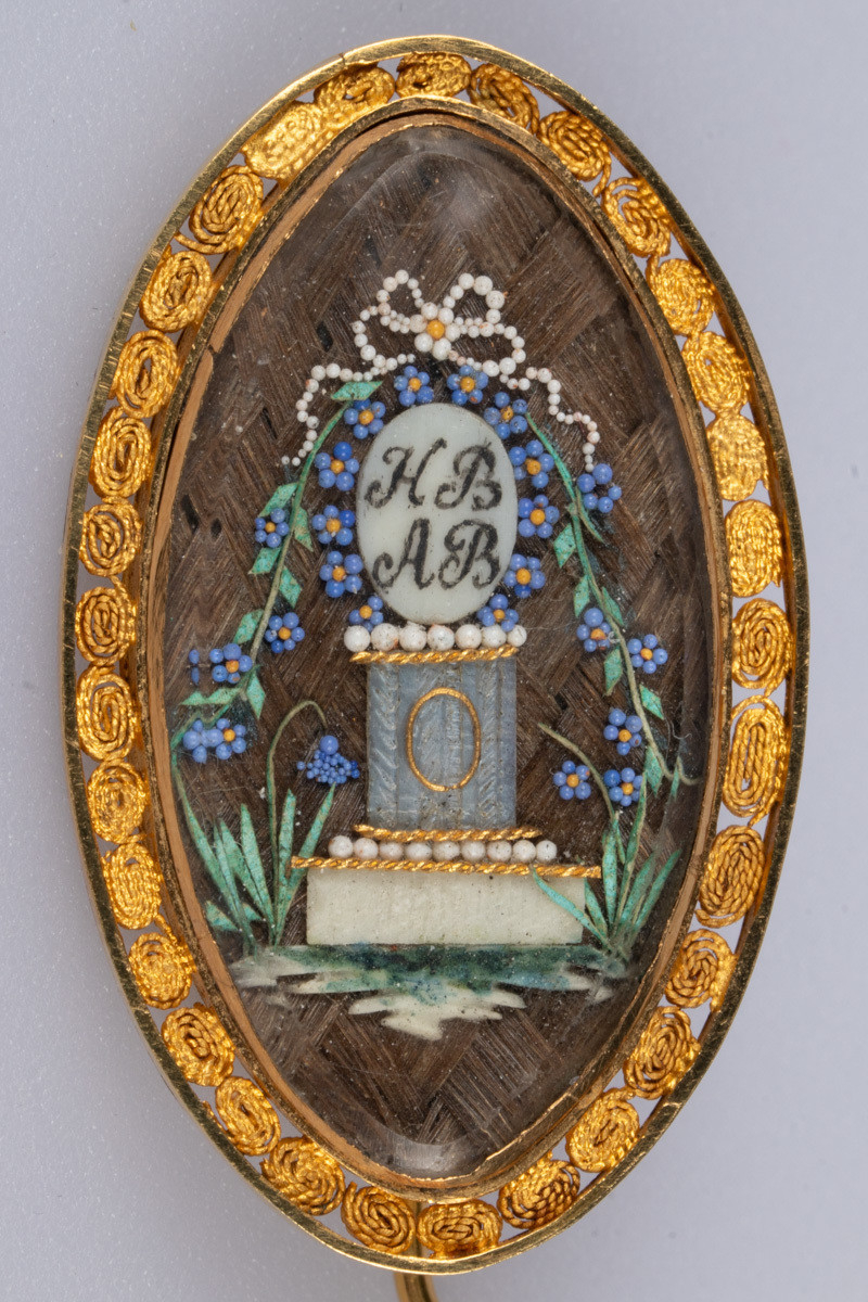 Minnestøtte/søyle med initialene til Henrik Dinclow Bruun og Anne Marlene Bruun . Perler formet som blå blomster, forglemmegei, og grønt gress rundt fundamentet på søylen