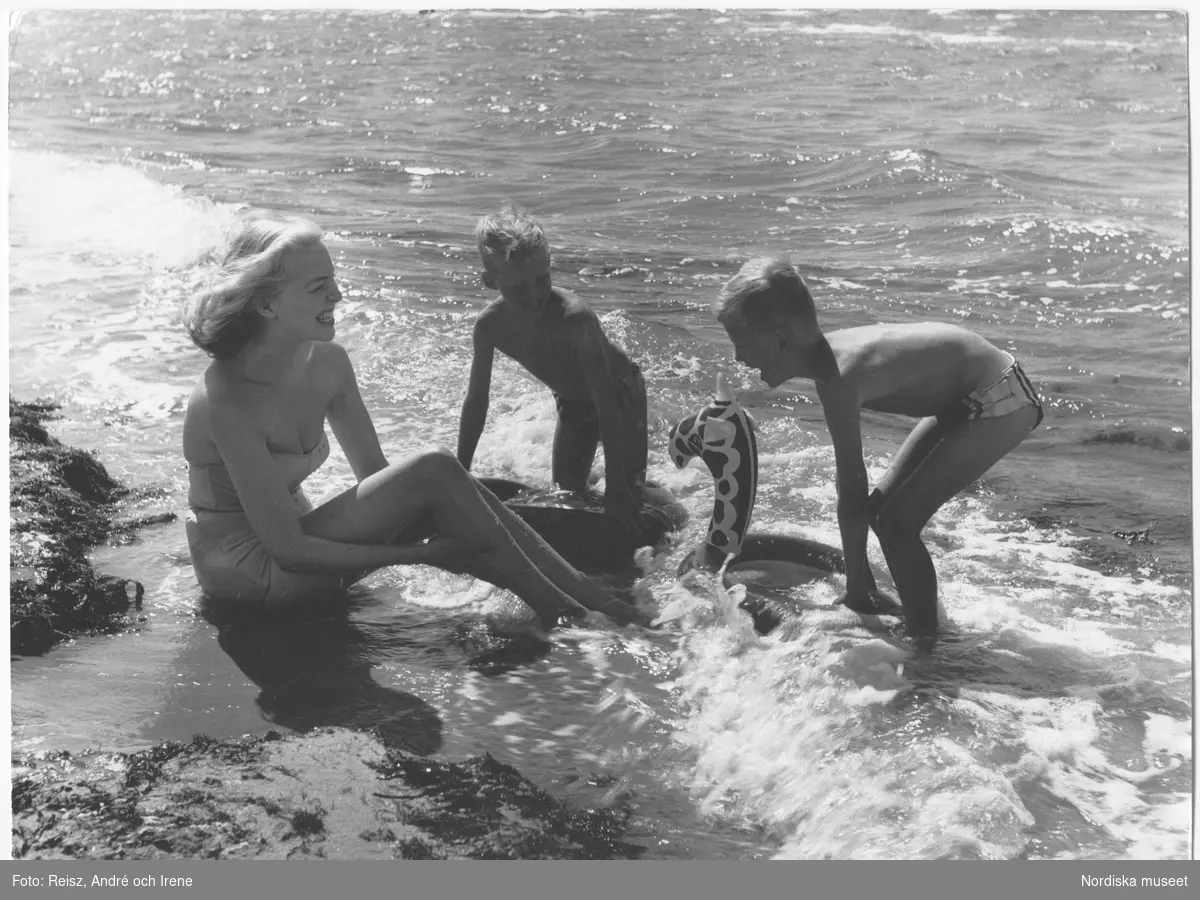 En kvinna och två pojkar med en badring badar i havet vid Tylösand strandbad.