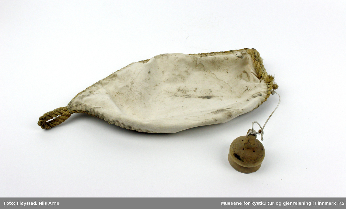 En oval bølgedemper, eller oljepose laget av lerret og sydd sammen med hampetau. Det er festet en trekork til å åpne og lukke posen. Trekorken er festet til en hvit tråd.