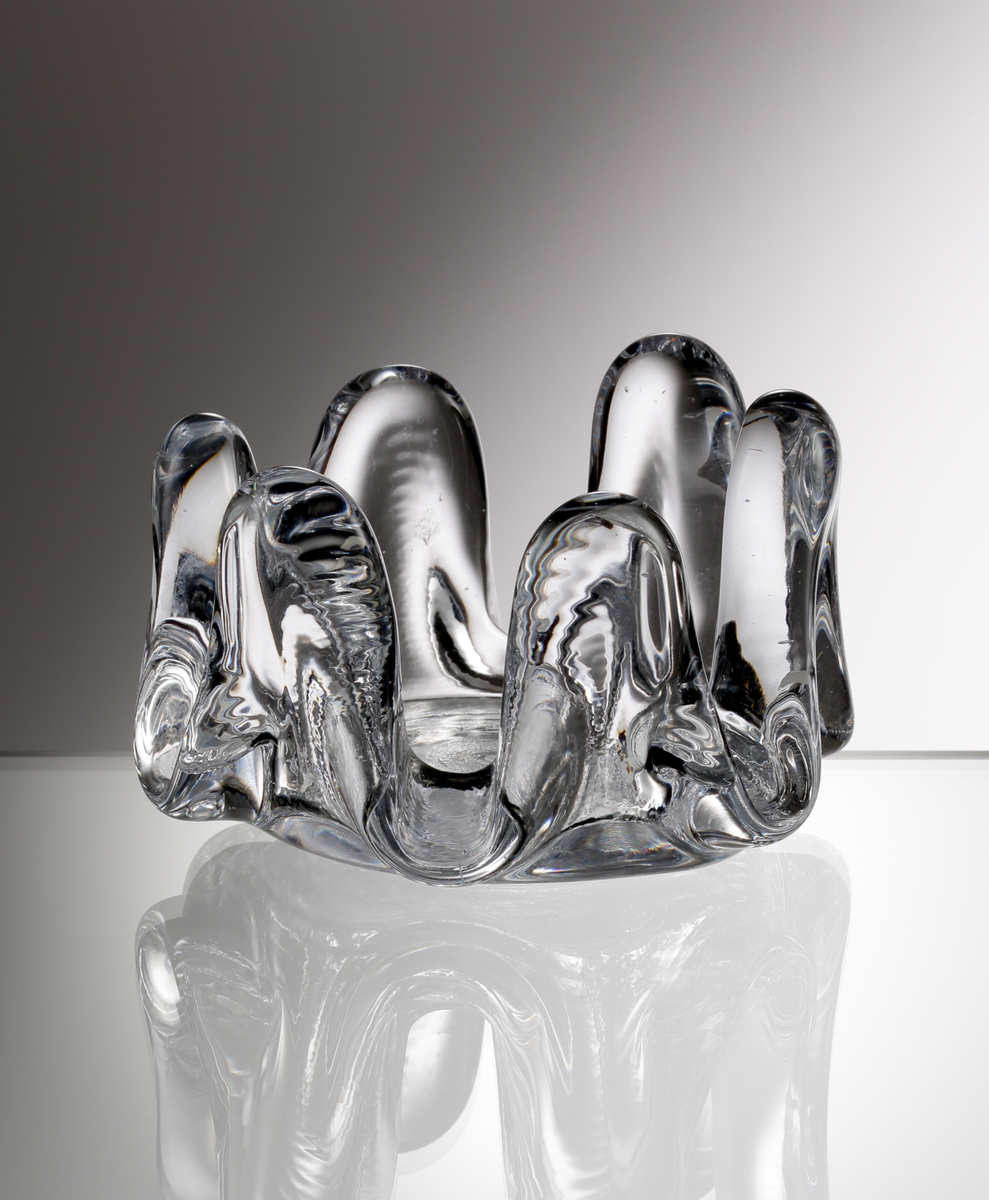 "Solros", formgiven av Göran och Ann Wärff. Ofärgat glas. Askfatet är delvis gjord i en hyttarbetad teknik som innebär att ovandelen, på den stiliserade blomman, har runnit ut av egen kraft. Därför blir alla glas i Solros-serien unika i sitt uttryck.