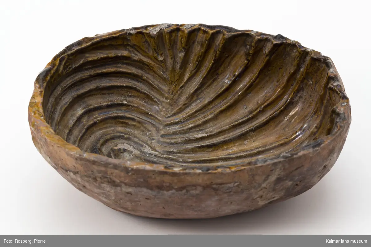 KLM 6663. Form, av keramik, lergods. Oval djup form med bredare och smalare fåror, inböjda från ena sidan, formen av en mussla. Invändigt glaserad. Gulbrun.