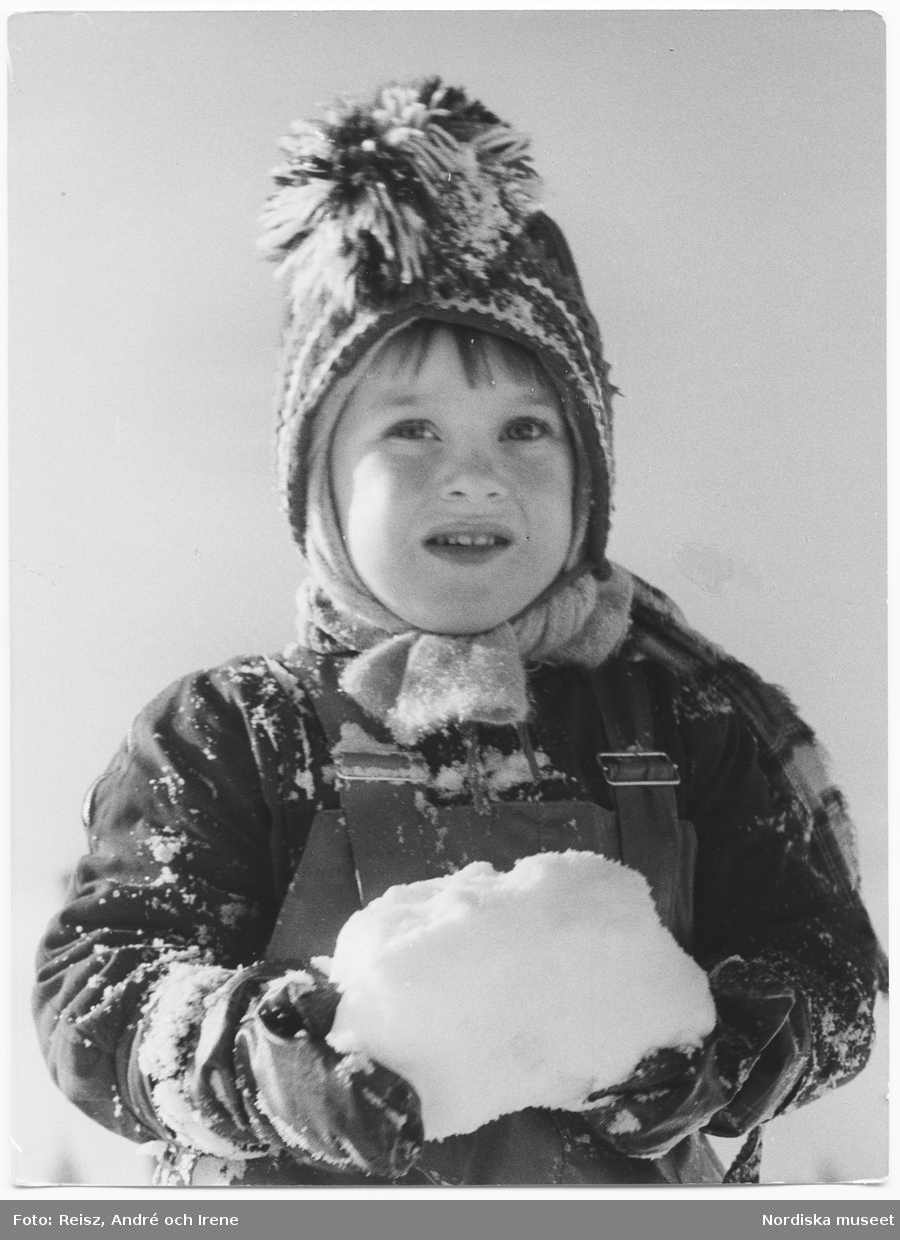 Porträtt av ett barn i vinterkläder som håller en snöboll i händerna.