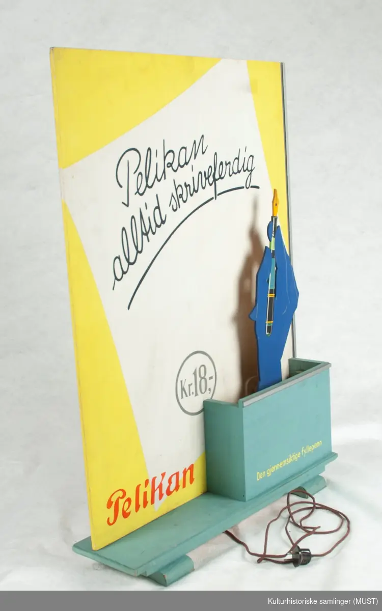 Reklameskilt for Pelikan kulepenner. Skiltet har en hengslet utsktrakt hånd i kryssfiner som drives av en elektromotor. 
