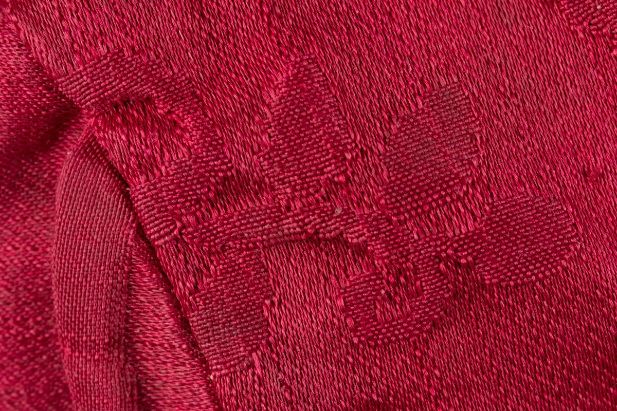 Liten, håndsydd dåpslue i rosa silkebrokade, med perleknipling i sydd med lintråd langs kanten. Sydd sammen av tre stykker tøy. Kantbånd i hvit silke, og blå silkebånd til knyting i halsen. Lua er foret med hvitt linlerret.