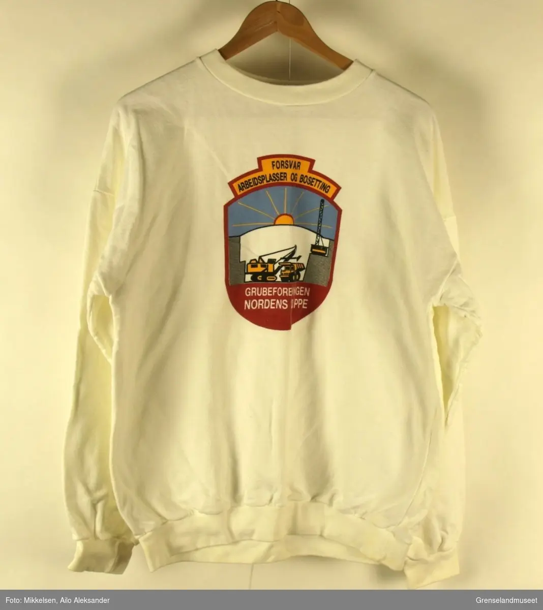Gjenstanden er en hvit skjorte med logoen til Grubeforeningen Nordens Klippe på forsiden og teksten "Grubeforeningen Nordens Klippe" på ryggen. 