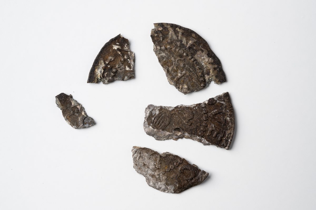 Fem fragment av ett ettöres silvermynt från 1600-talet. Samtliga fragment från myntet finns inte kvar.