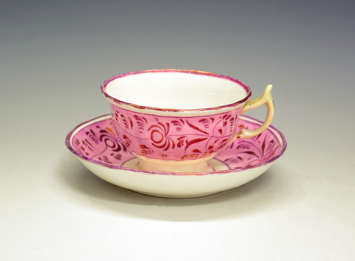 Fra protokollen: Tekopp med skål. Dekor i form av en frise med lys rød bunnfarge og påmalte blomsterranker i gull. Uten merke. Engelsk luster-keramikk  (lustreware/lusterware).