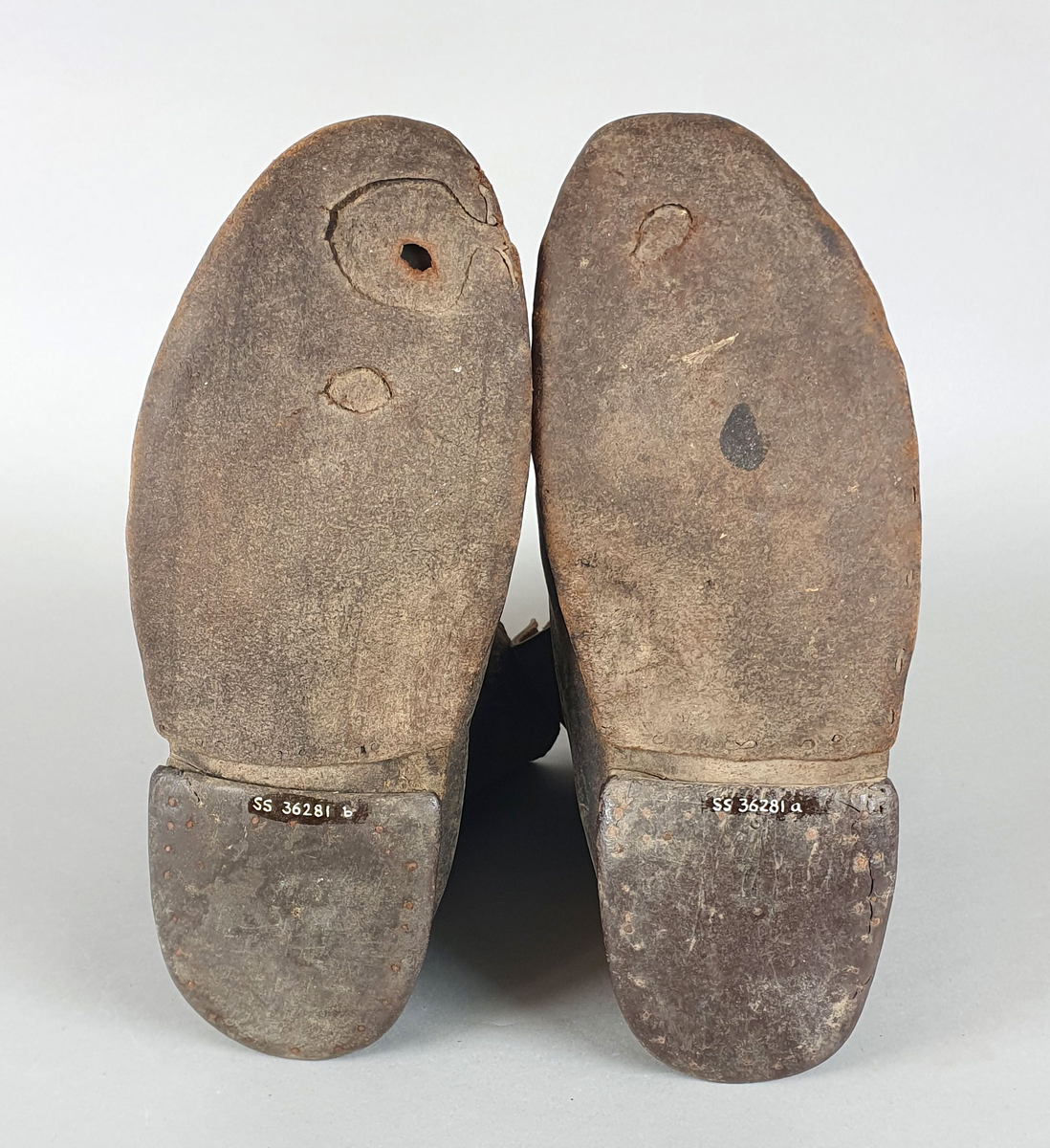 Et par støvler av skinn. Skinnet er sydd sammen på framsidene. Støvlene er påsatt halvsåle av lær og hæl av lær og gummi.