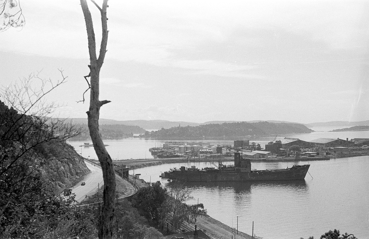 Oslo havn, sett sørover mot Bunnefjorden. Sjursøya i forgrunnen med skip ankret opp. Ormøya (med kirkespir) og Malmøya midt i bildet. Nesoddlandet i bakgrunnen. Mosseveien og jernbanen foran til venstre. Fartøyet på fotografiet, som sannsynligvis er tatt i 1948, er den tidligere tyske Sperrbrecher 33, en form for minesveiper, før tilbakeføring til lastebåt.