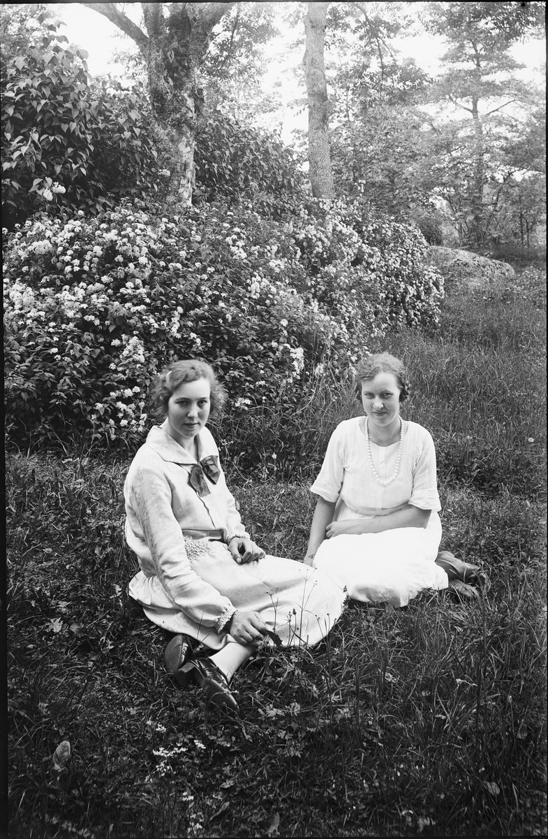 Två unga kvinnor sitter i trädgård, Alunda, Uppland