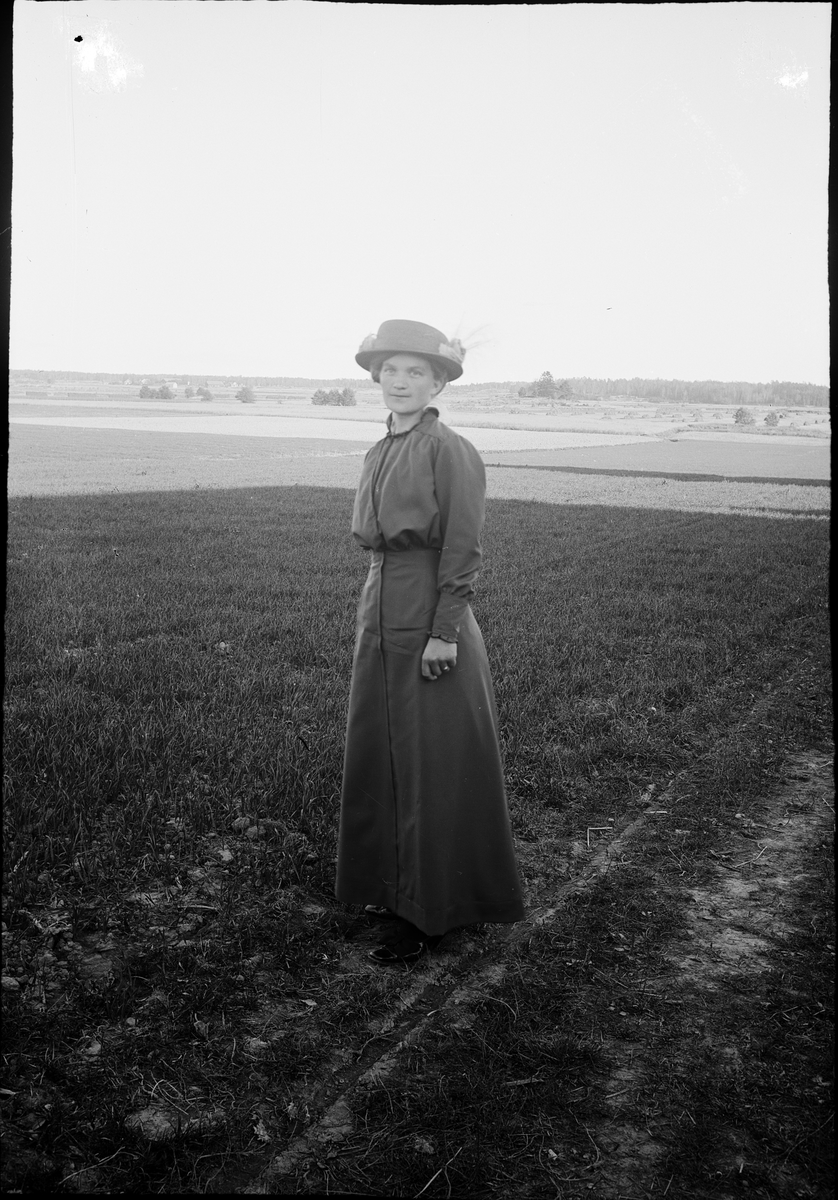Kvinna ståendes ute i odlingslandskap, Alunda, Uppland