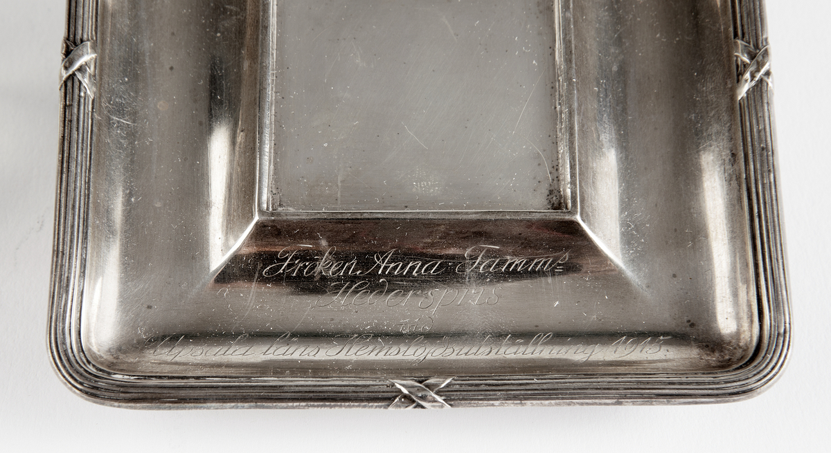 FAt av silver av silver med inskriften "Fröken Anna Tamms Hederspris vid Uppsala läns hemslöjdsutställning 1915.