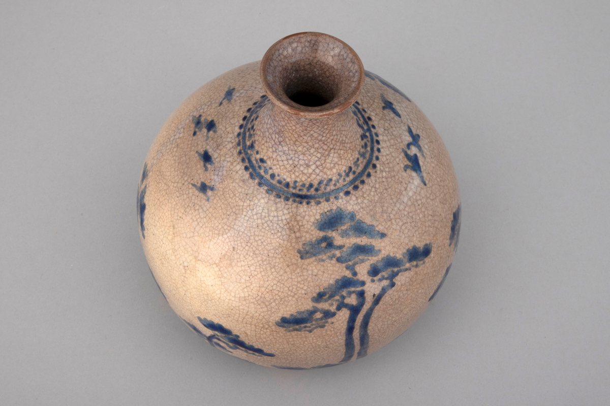 Vase i dreiet keramikk. Gråbrun glasur med krakeleringer. Dekor i blå overglasurmaling. Glasuren dekker ikke fotrandens underside. Dekoren viser motiv med stiliserte tre.