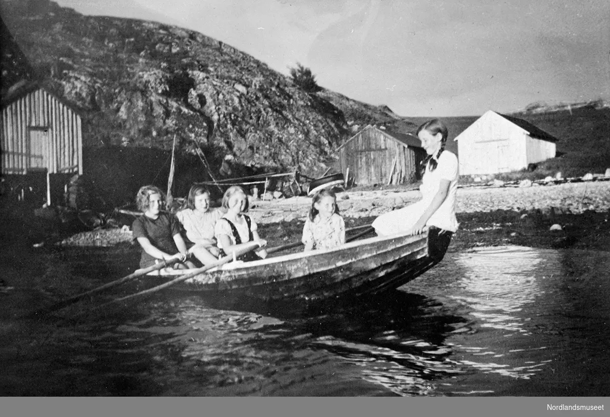En snekke med 5 jenter ombord. Fra venstre: Gerd Dahle, Svanhild Hoff (Hestøy), Maria Dahle (Rissa), Olga Hoff (Hestøy) og Anny Hoff (Hestøy). Tre naust på land, et av dem med brygge. Stedet er Breivik i Rangsund.
