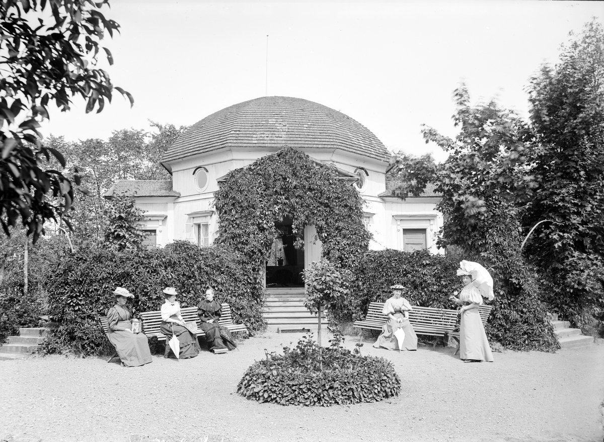 Framför den originella paviljongen i Wallenbergska trädgården i Linköping, sitter ett sällskap som ännu inte identifierats. Utifrån andra fotografier är en rimlig datering år 1898.