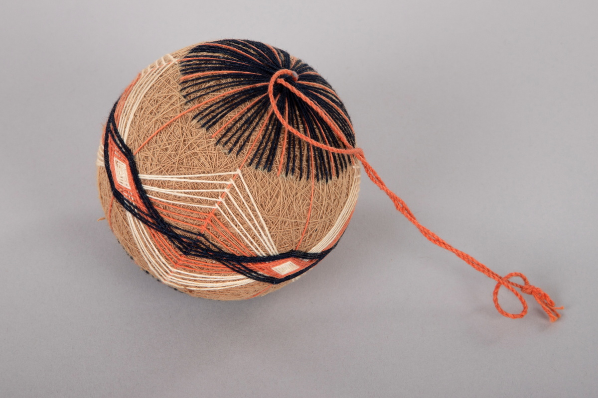 Ball med, antagelig, en kjerne av hardpresset papp eller papir omviklet og brodert med bomullstråd i flere lag. Hvert lag danner et mønster. Opphengssnor i toppen.

