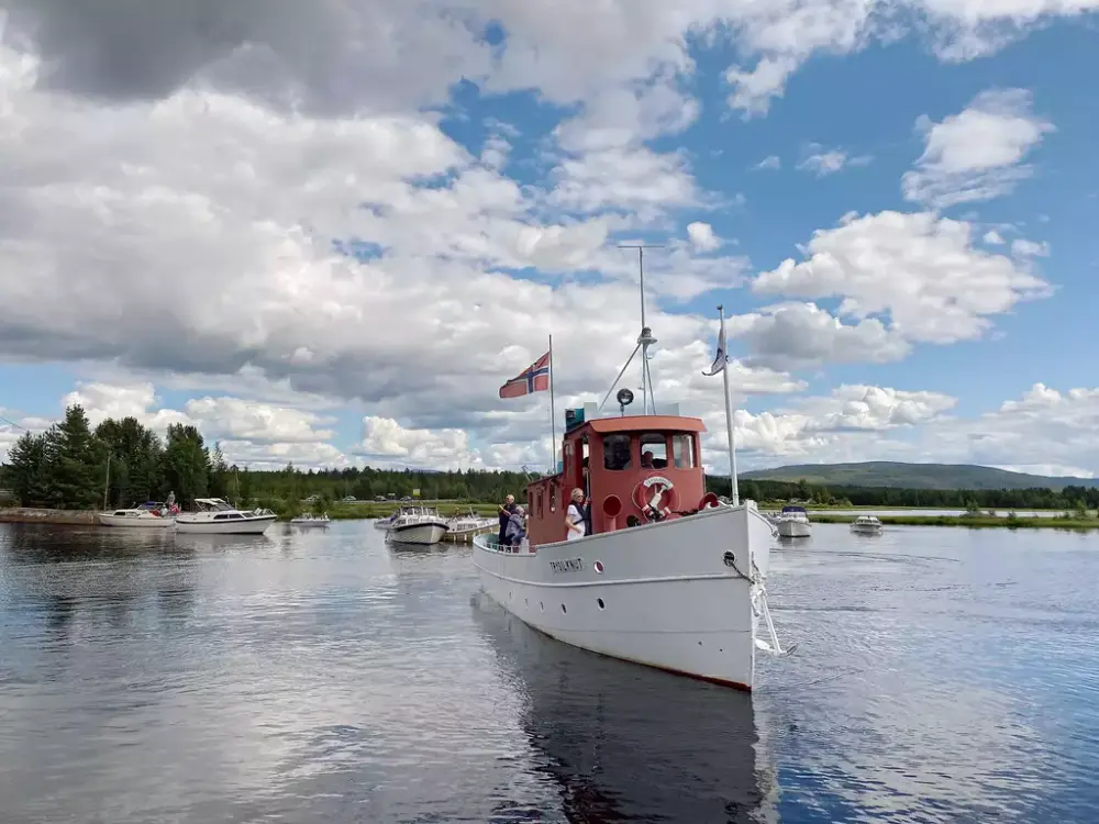 En båt som seiler mot kameraet, småbåter på vannet i bakgrunnen.