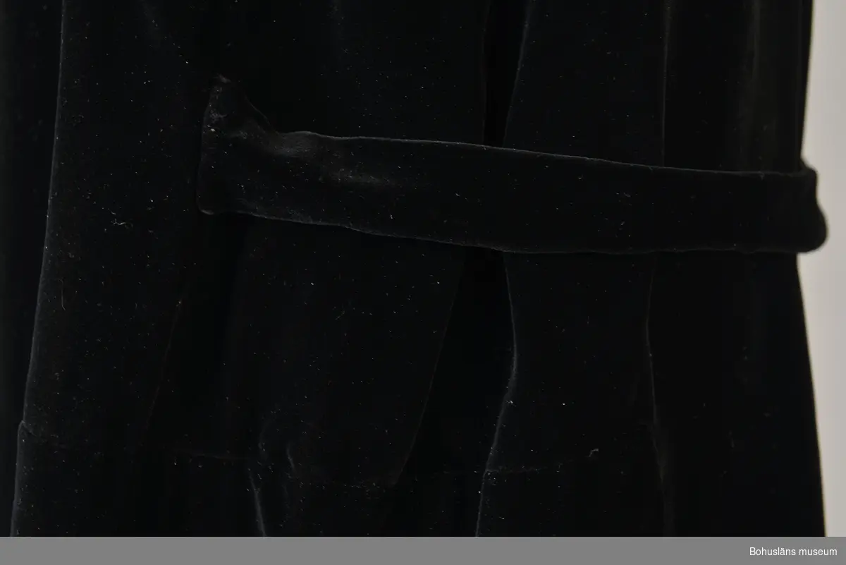 Kappa i svart sammet med vitt sidenfoder. Pellerinkrage och löst sittande skärp.