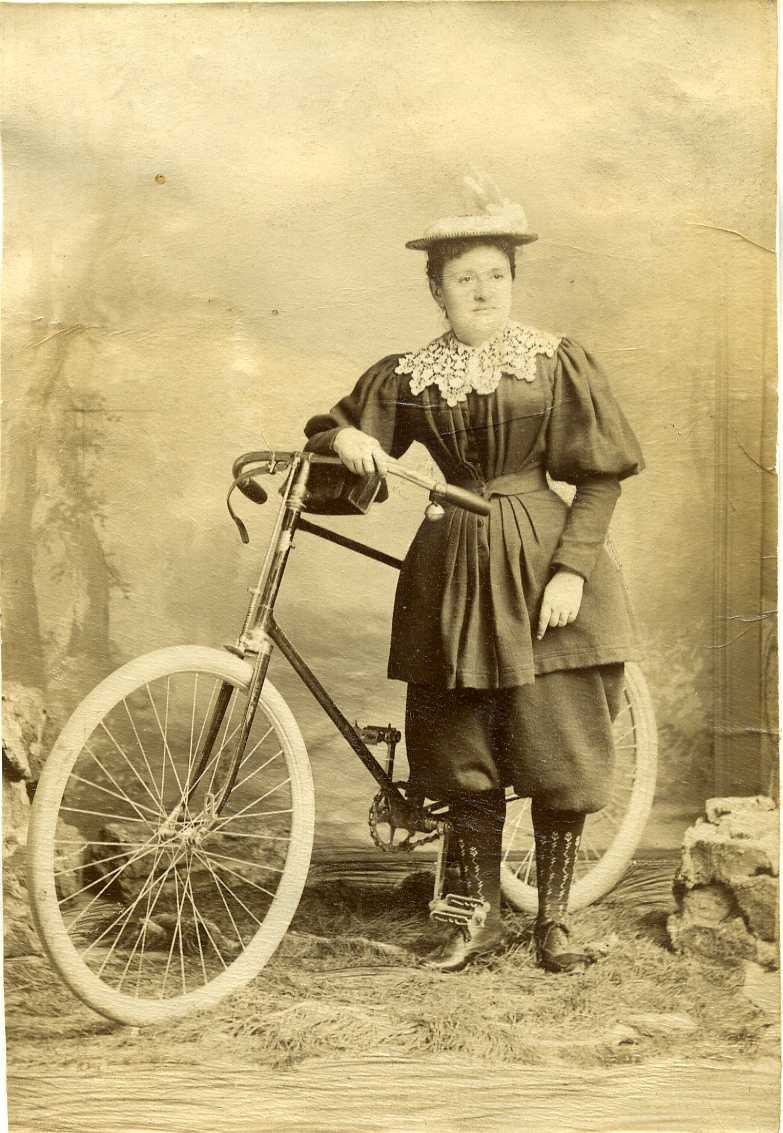Porträtt av en ung kvinna som står vid en cykel - ateljéfoto.